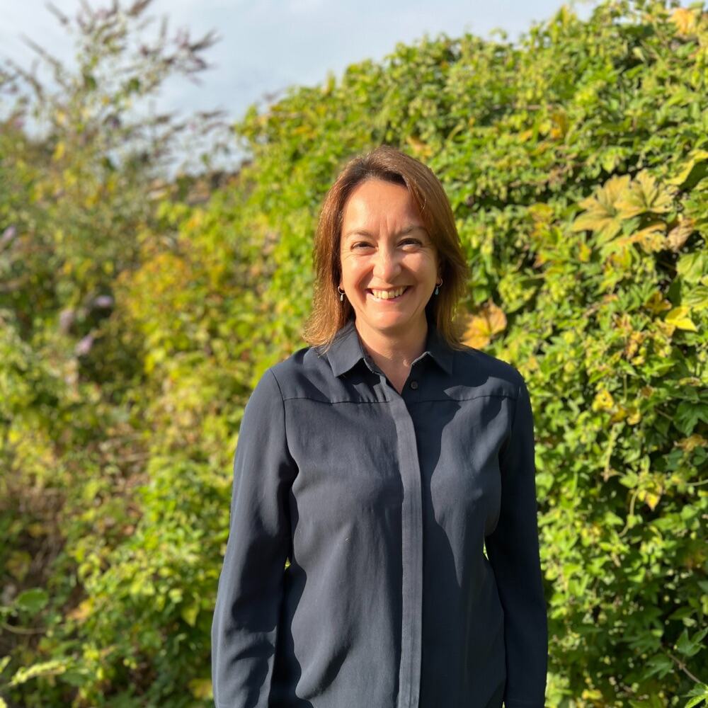 Donna, co-founder of Mini Makers, smiling in front of a hedge