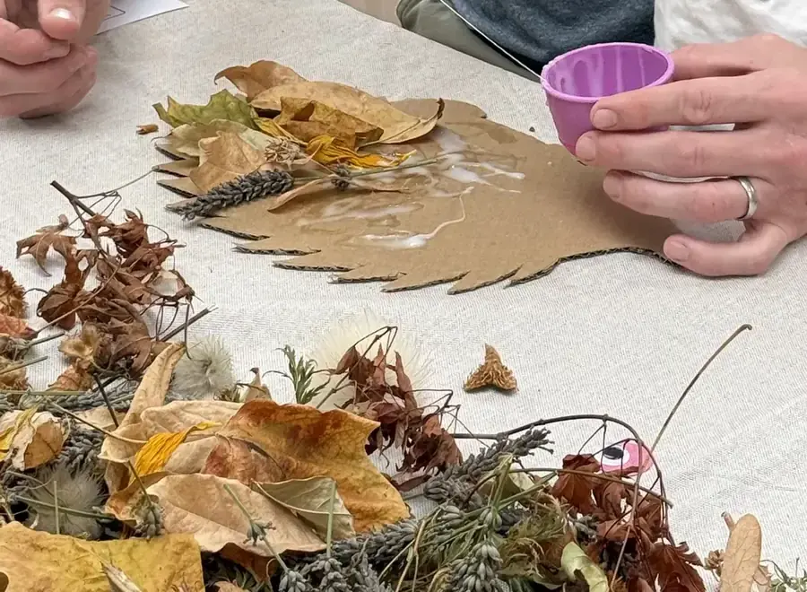 A grown-up and a child gluing leaves onto a hedgehog collage