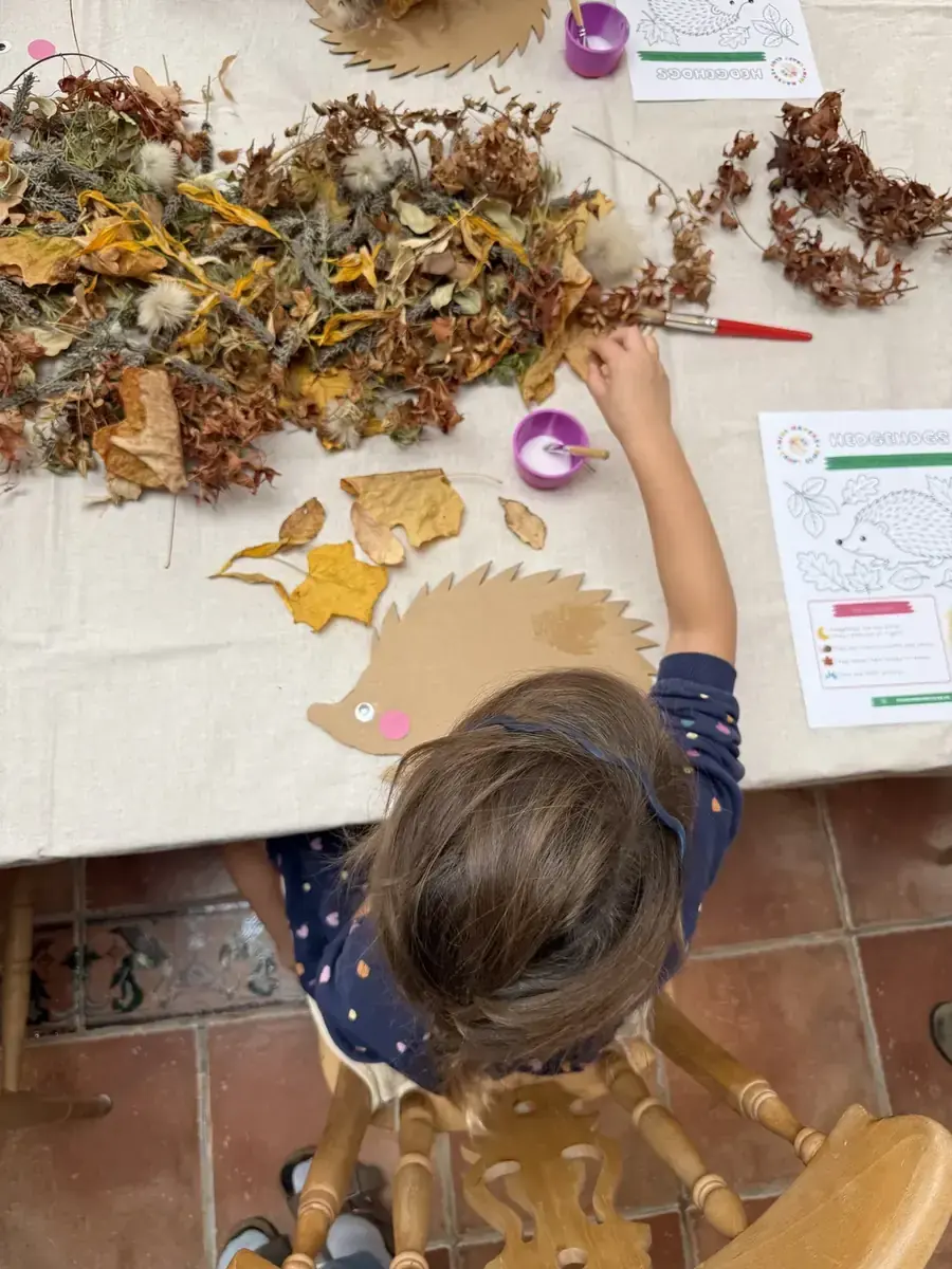 A child adding autumn leaves to a cardboard hedgehog, seen from above