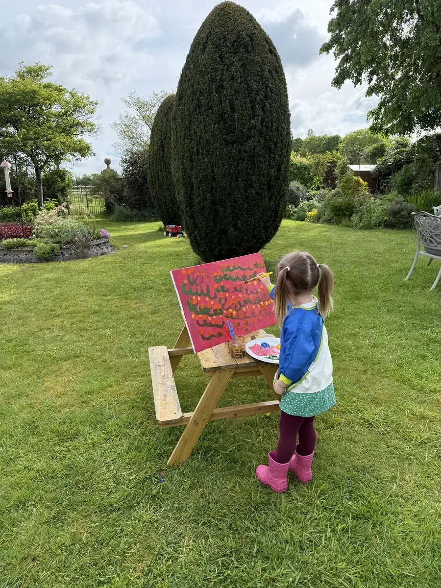 A child painting a bright picture at an easel in the garden