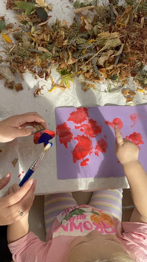 Small hands printing red paint onto purple paper