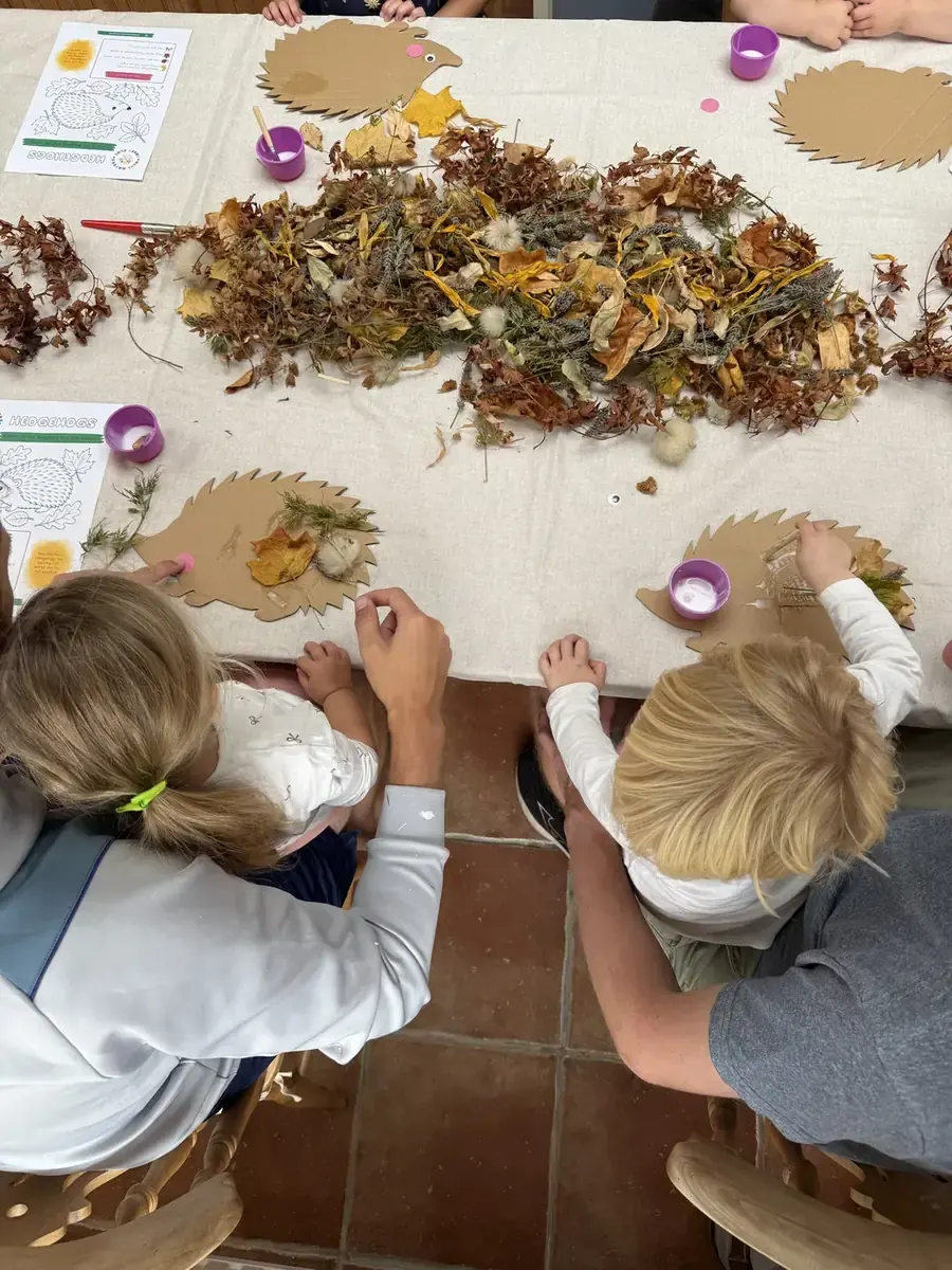 Two children decorating cardboard hedgehogs with a grown-up helping